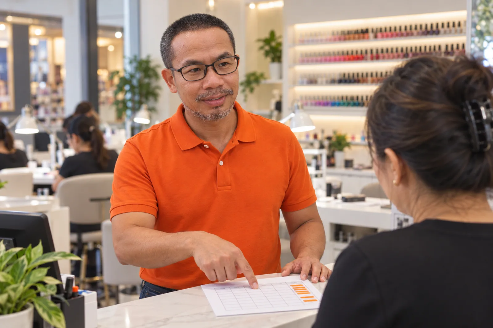 Hai Pham points at the Sunday column of a salon roster while talking it through with a salon owner at the counter